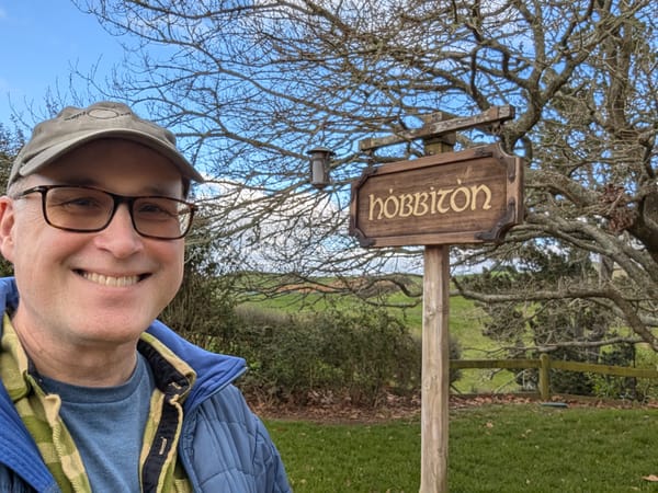 The bespeckled author standing in front of the town sign of Hobbiton
